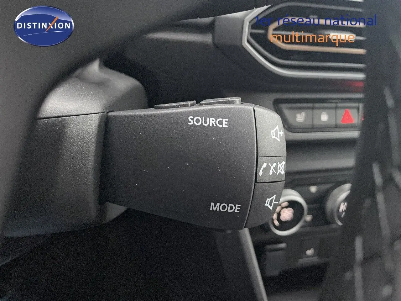 Gros plan sur la commande audio au volant du Dacia Jogger gris schiste, avec tableau de bord et commandes clim visibles en arrière-plan.