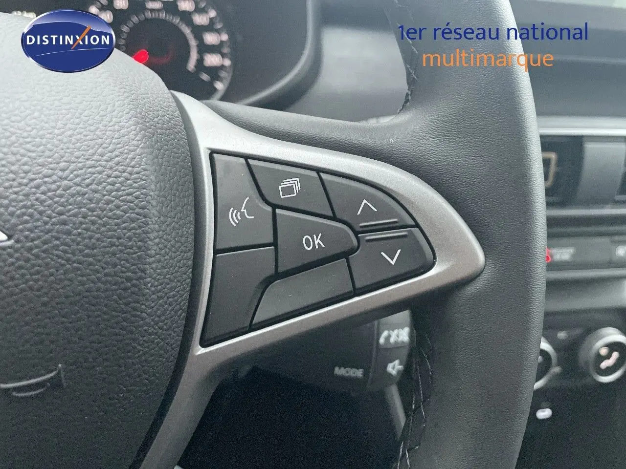 Gros plan sur le volant multifonction noir du Dacia Jogger 2026, avec commandes audio et affichage au tableau de bord flou.