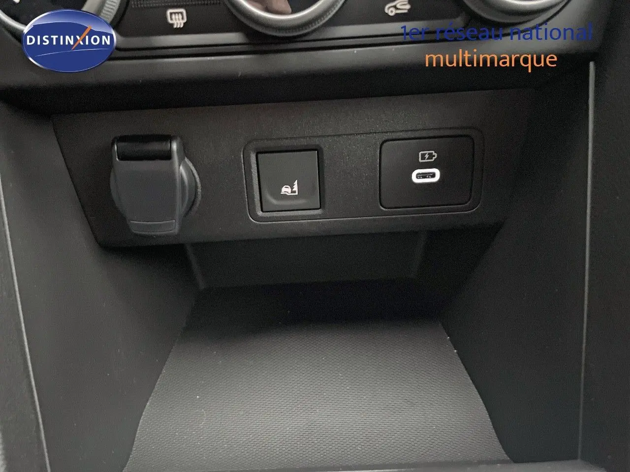 Gros plan sur la console centrale du Dacia Jogger gris schiste, montrant prises USB et bouton d'assistance au stationnement.