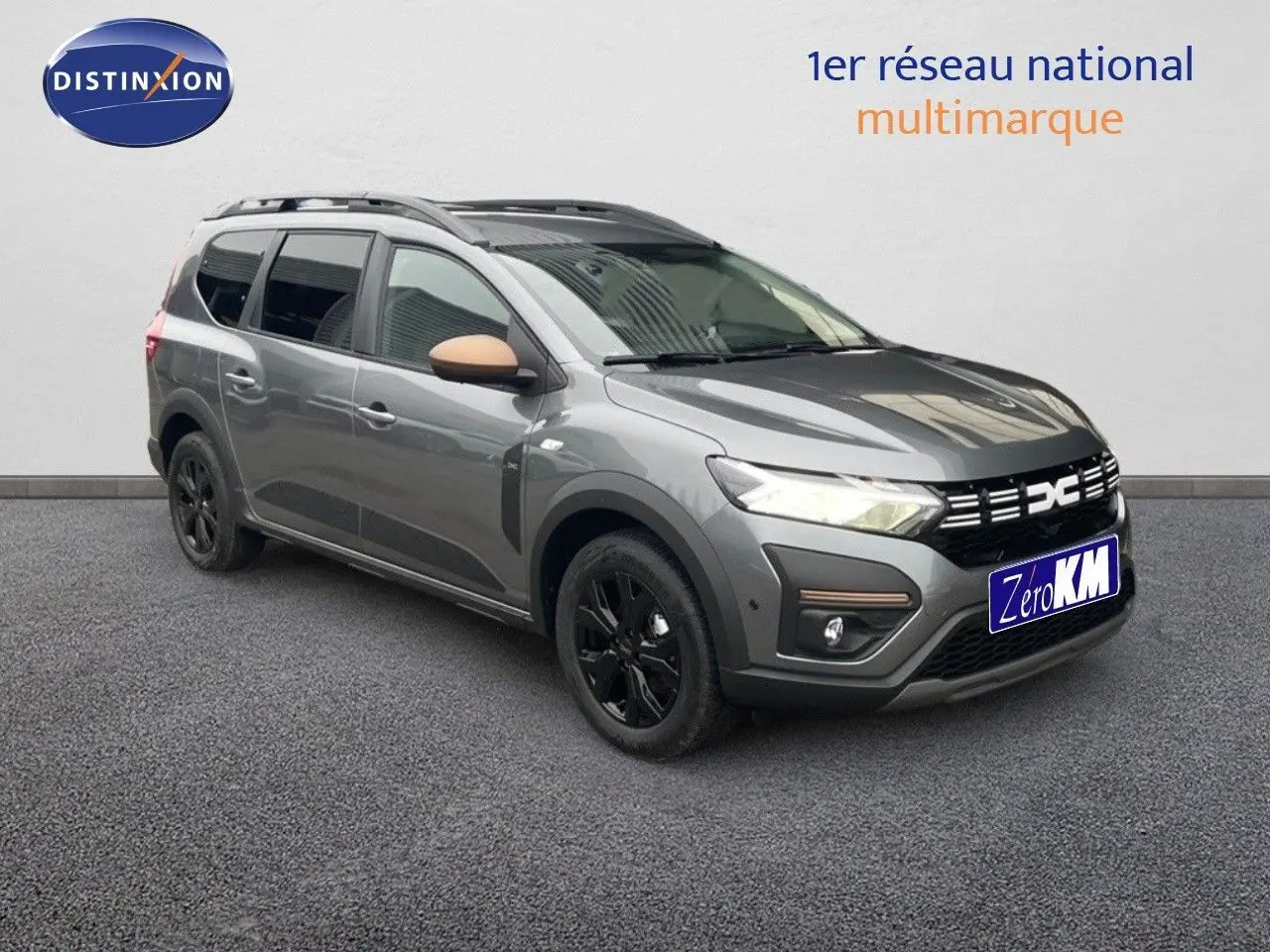 Dacia Jogger gris schiste métal en 3/4 avant droit, avec jantes noires et coques de rétroviseur beige.