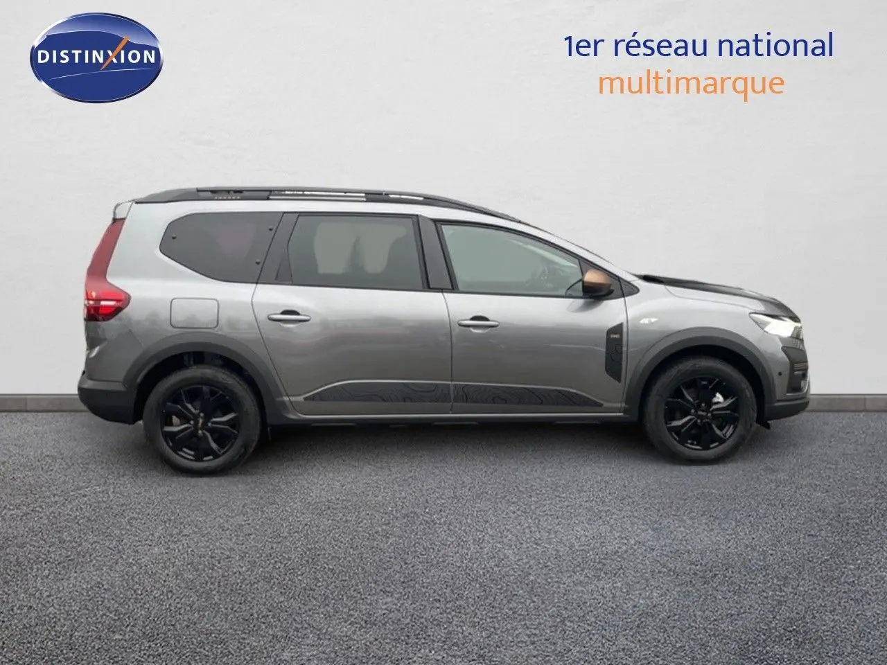 Vue latérale droite d'un Dacia Jogger gris schiste métallisé avec jantes noires et barres de toit, sur fond neutre.