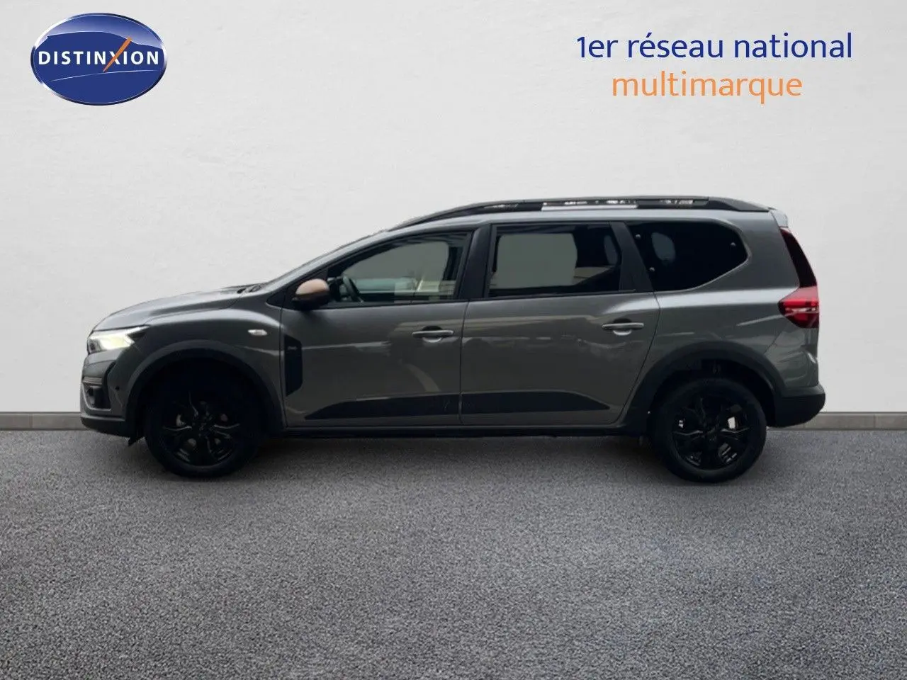 Profil latéral droit du Dacia Jogger gris schiste métal 7 places avec jantes noires et barres de toit visibles.