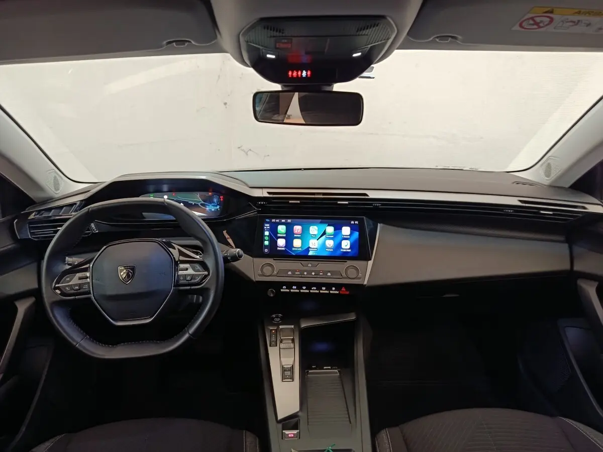 Vue intérieure avant de la Peugeot 308 2023, tableau de bord noir avec écran tactile central lumineux et volant cuir multifonctions.