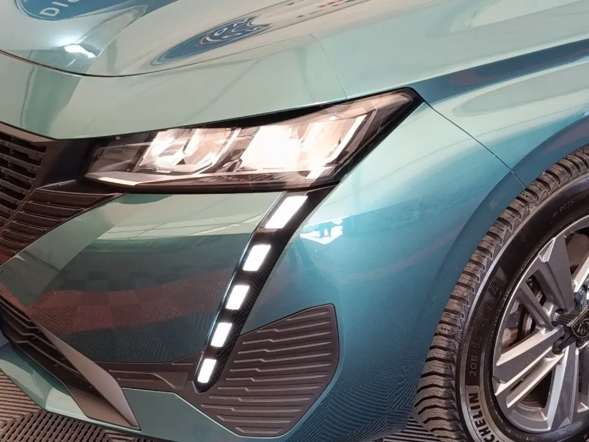 Gros plan sur l'avant droit bleu métallisé du Peugeot 308 2023, mettant en valeur les phares LED et la jante alliage.
