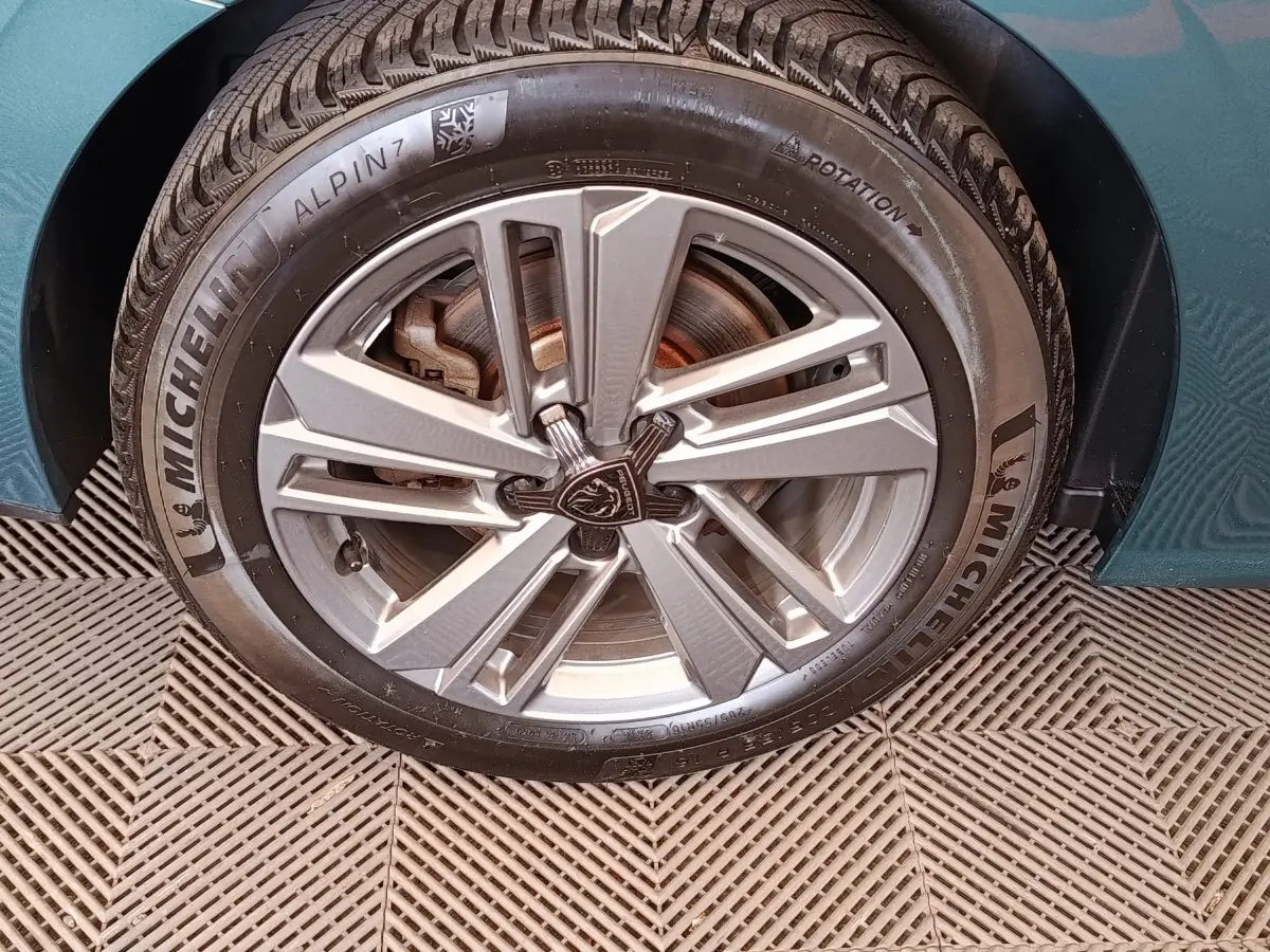 Gros plan sur la roue avant gauche d'une Peugeot 308 2023 bleu vert avec jante alliage et pneu Michelin Alpin 7.