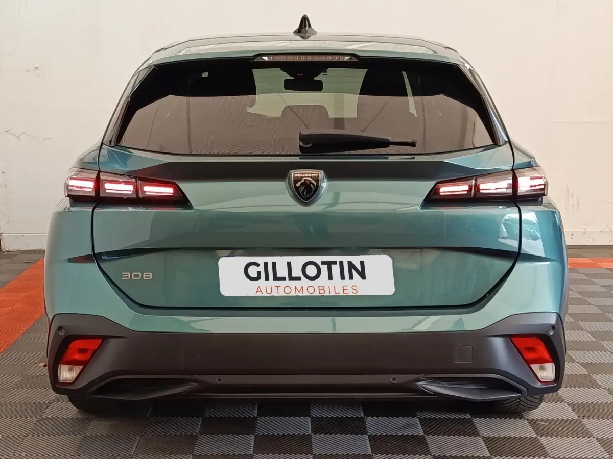 Vue arrière d'une Peugeot 308 2023 vert métallisé avec feux LED allumés et logo lion central sur hayon.