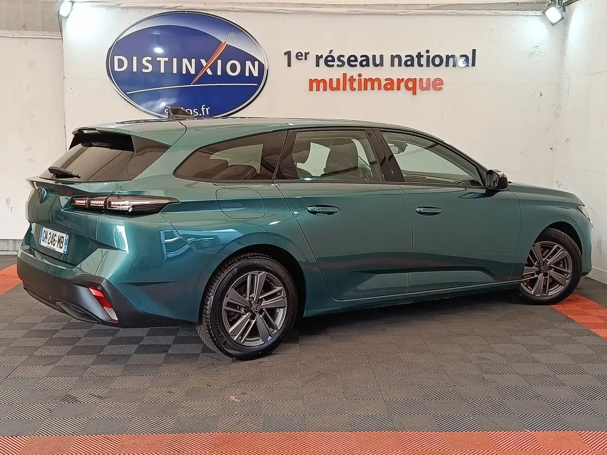 Peugeot 308 break 2023 vert métallisé vue 3/4 arrière côté droit en intérieur showroom.