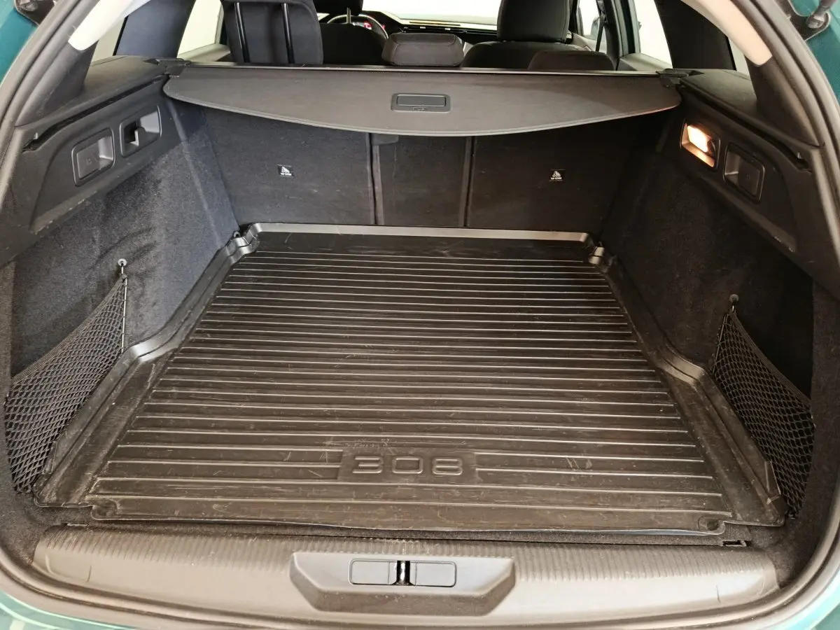 Vue intérieure du coffre noir d'une Peugeot 308 2023 avec tapis de protection et filets latéraux de rangement.