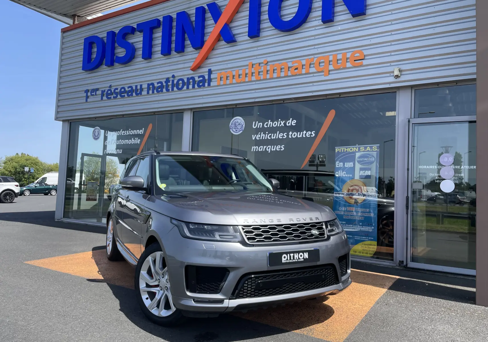 Range Rover Sport gris Eiger en 3/4 avant droit, avec jantes alu 21 pouces devant un showroom Distinxion.