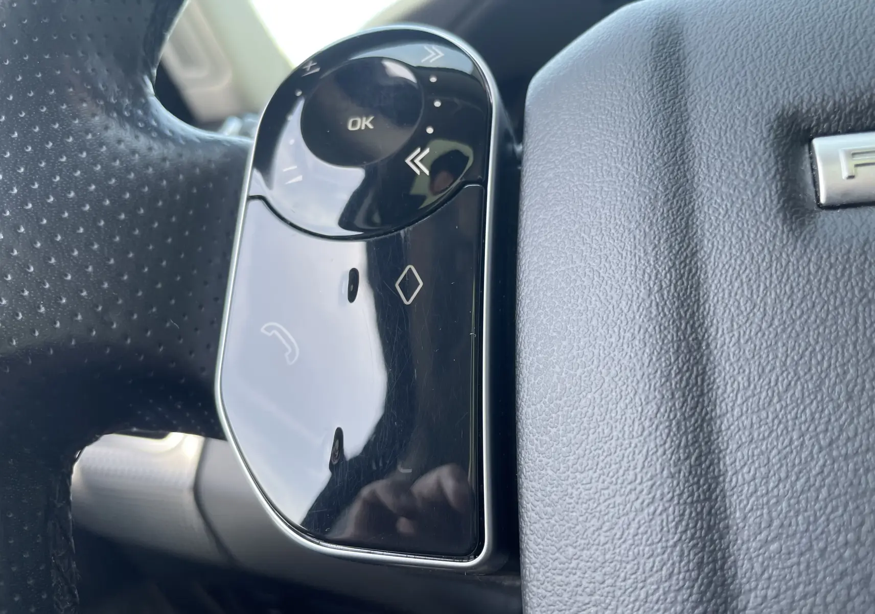 Gros plan sur les commandes gauche du volant en cuir noir du Range Rover Sport gris, avec boutons multifonctions brillants.