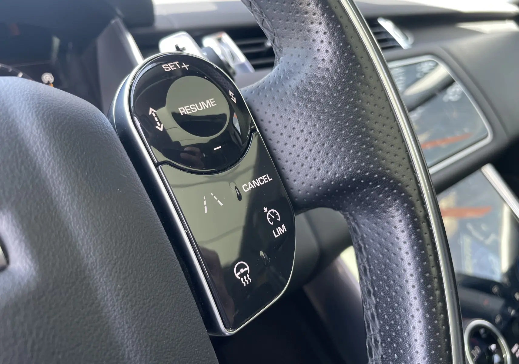 Gros plan sur le volant en cuir noir du Range Rover Sport gris, avec commandes de régulateur de vitesse et assistant de voie.