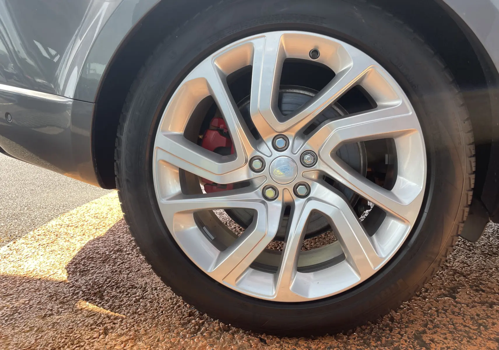 Gros plan sur la jante alu 21 pouces argentée et le frein rouge du Range Rover Sport gris Eiger côté arrière.