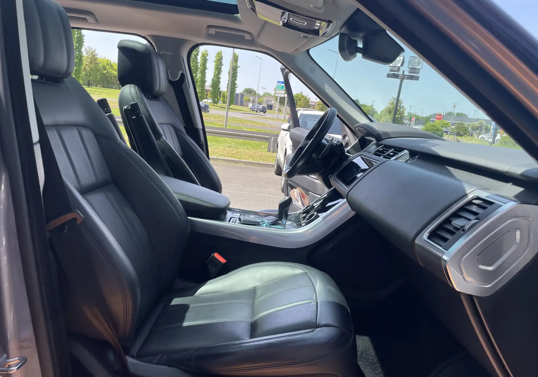 Intérieur noir cuir du Range Rover Sport gris, vue côté conducteur avec tableau de bord et console centrale visibles.