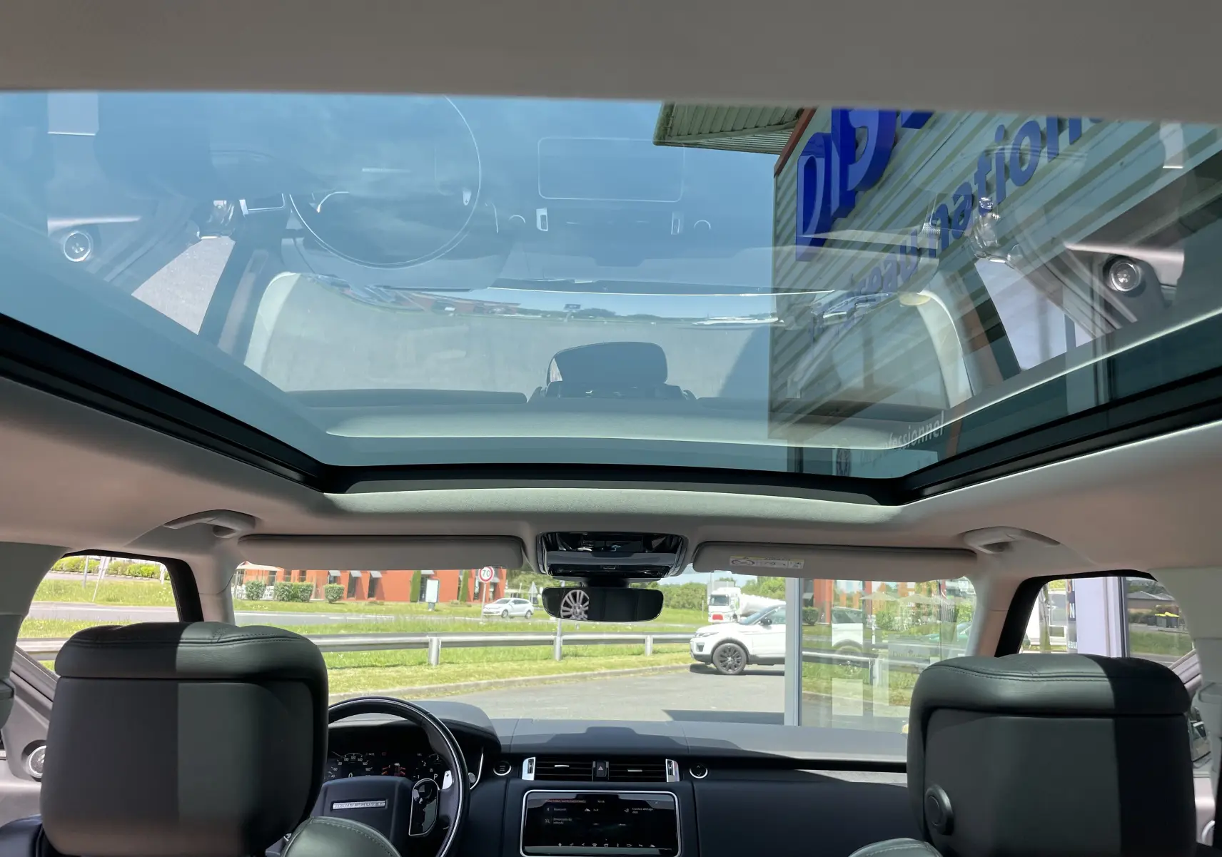Vue intérieure du toit panoramique et tableau de bord du Range Rover Sport gris Eiger avec sellerie cuir noir.
