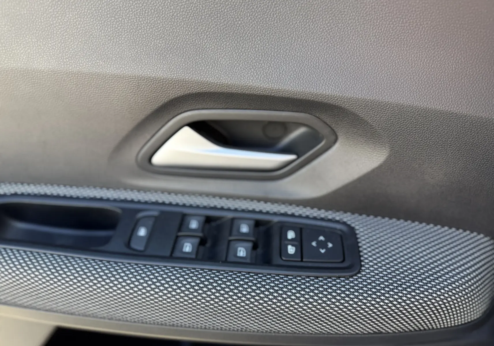 Gros plan sur la poignée intérieure et les commandes des vitres côté gauche d'une porte de Dacia Sandero Stepway gris schiste.