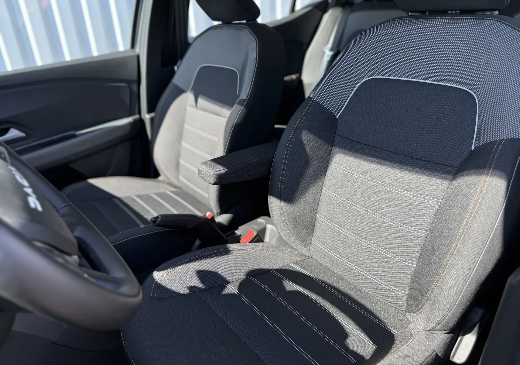 Gros plan sur les sièges avant en tissu gris et noir du Dacia Sandero Stepway 2025, avec accoudoir côté droit visible.