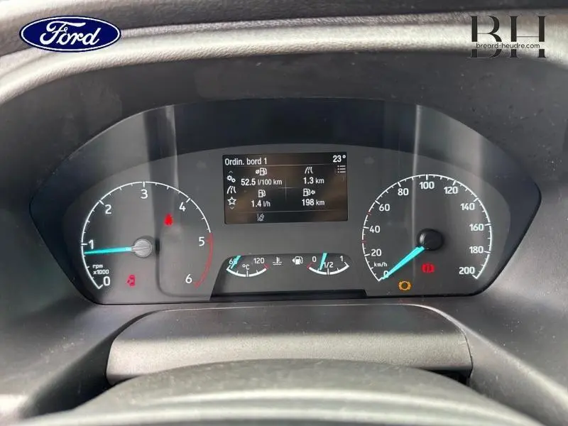 Vue rapprochée du tableau de bord numérique du Ford Transit Custom blanc, affichant compte-tours, vitesse et informations de bord.