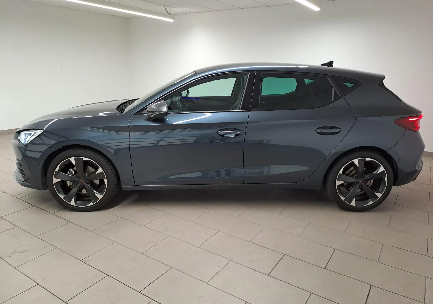 Profil côté gauche d'une CUPRA Leon 1.5 eTSI 150 ch gris magnétique 2023 avec jantes noires distinctives.