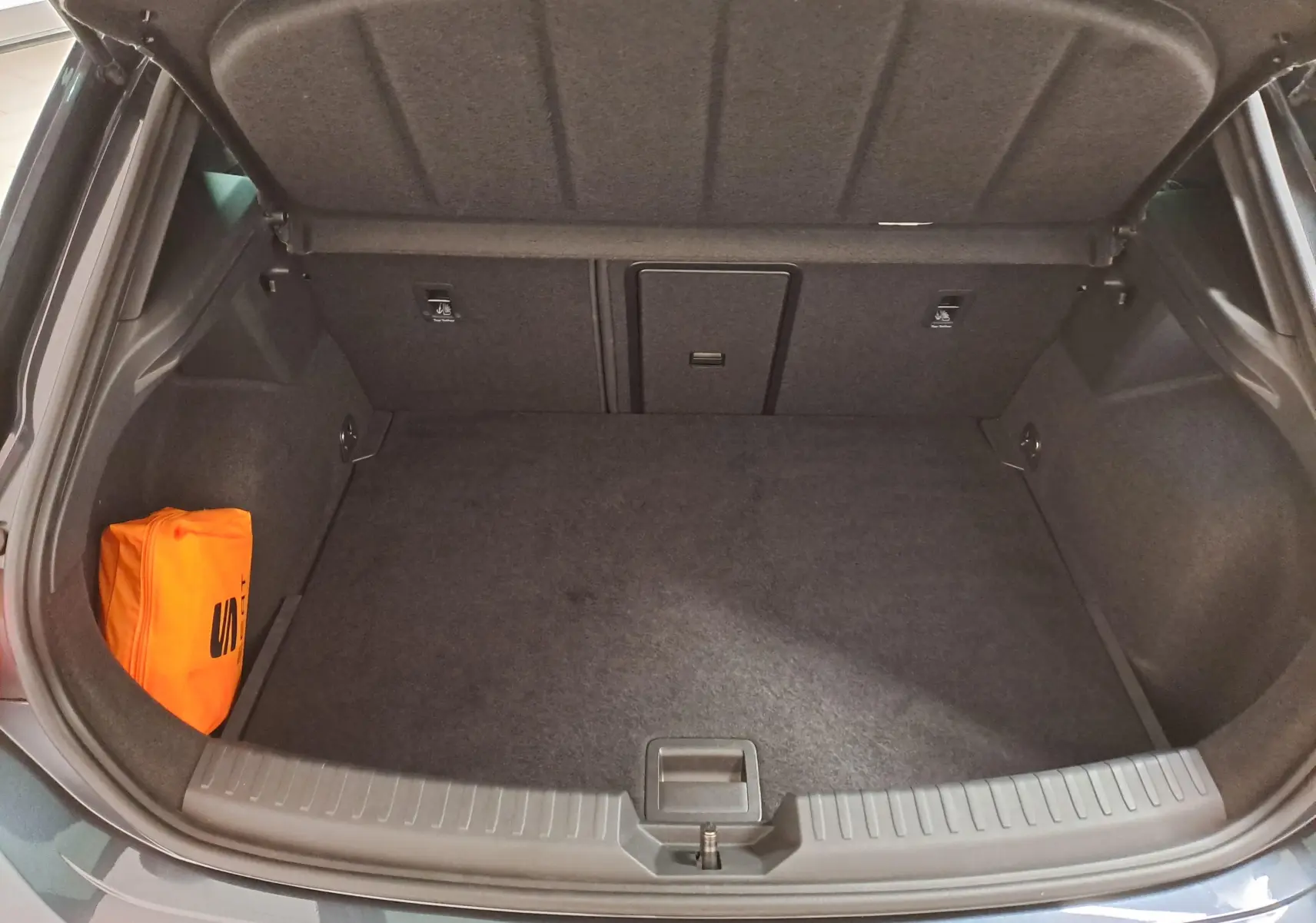 Coffre ouvert d'une CUPRA Leon 2023 gris magnétique, montrant un espace de rangement propre avec un kit de sécurité orange.