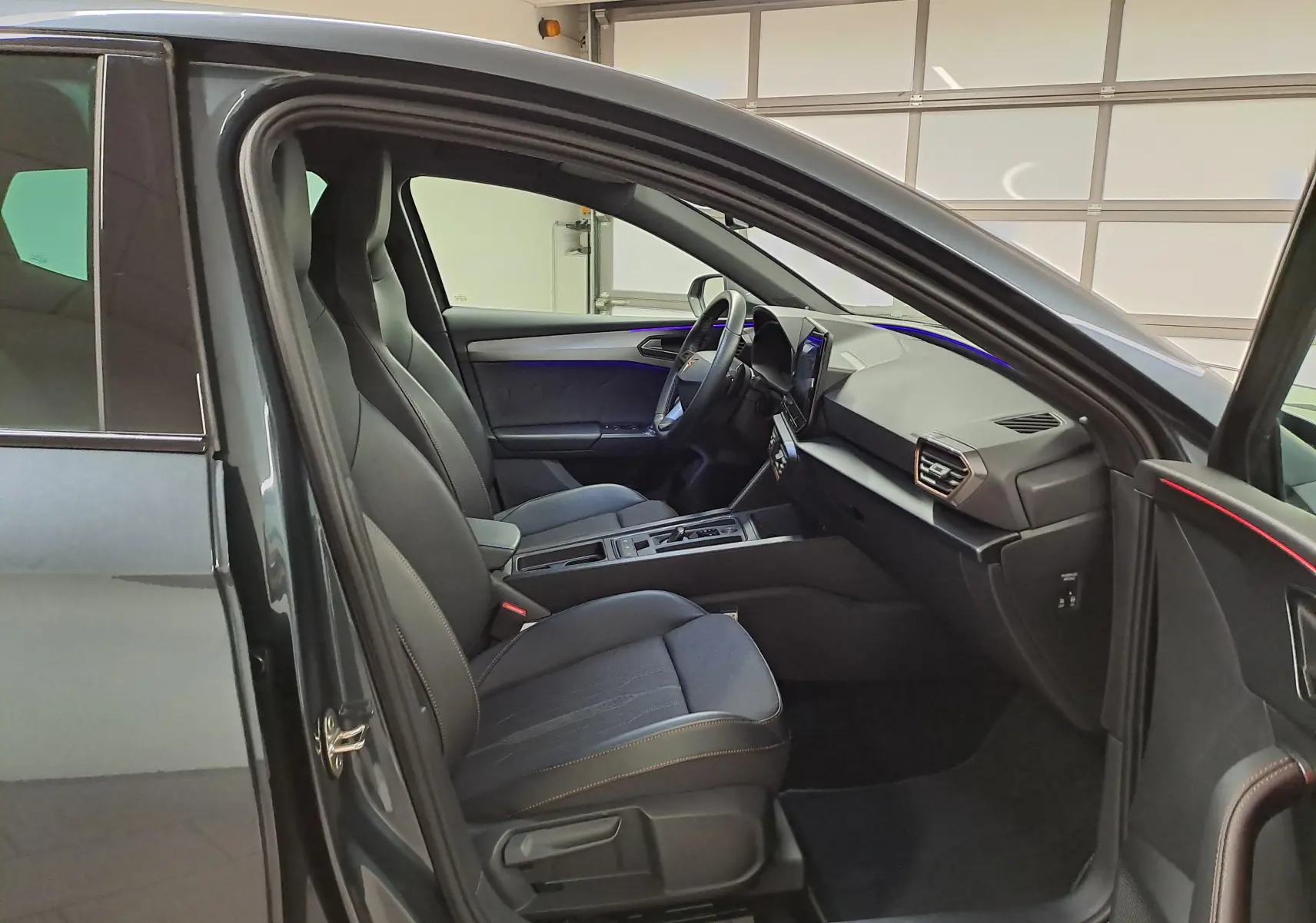 Intérieur avant droit d'une CUPRA Leon 1.5 eTSI 2023 gris magnétique, sièges sport et éclairage d'ambiance violet.