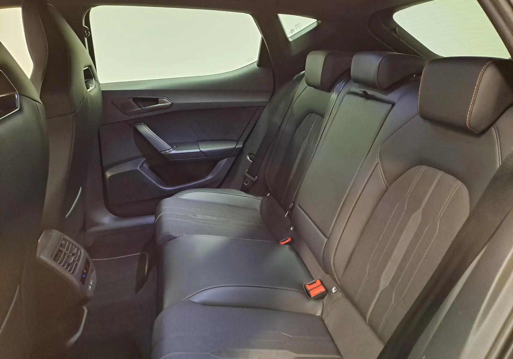 Vue intérieure arrière du CUPRA Leon 1.5 eTSI 2023 avec sièges noirs en cuir et surpiqûres orange, ambiance moderne et épurée.