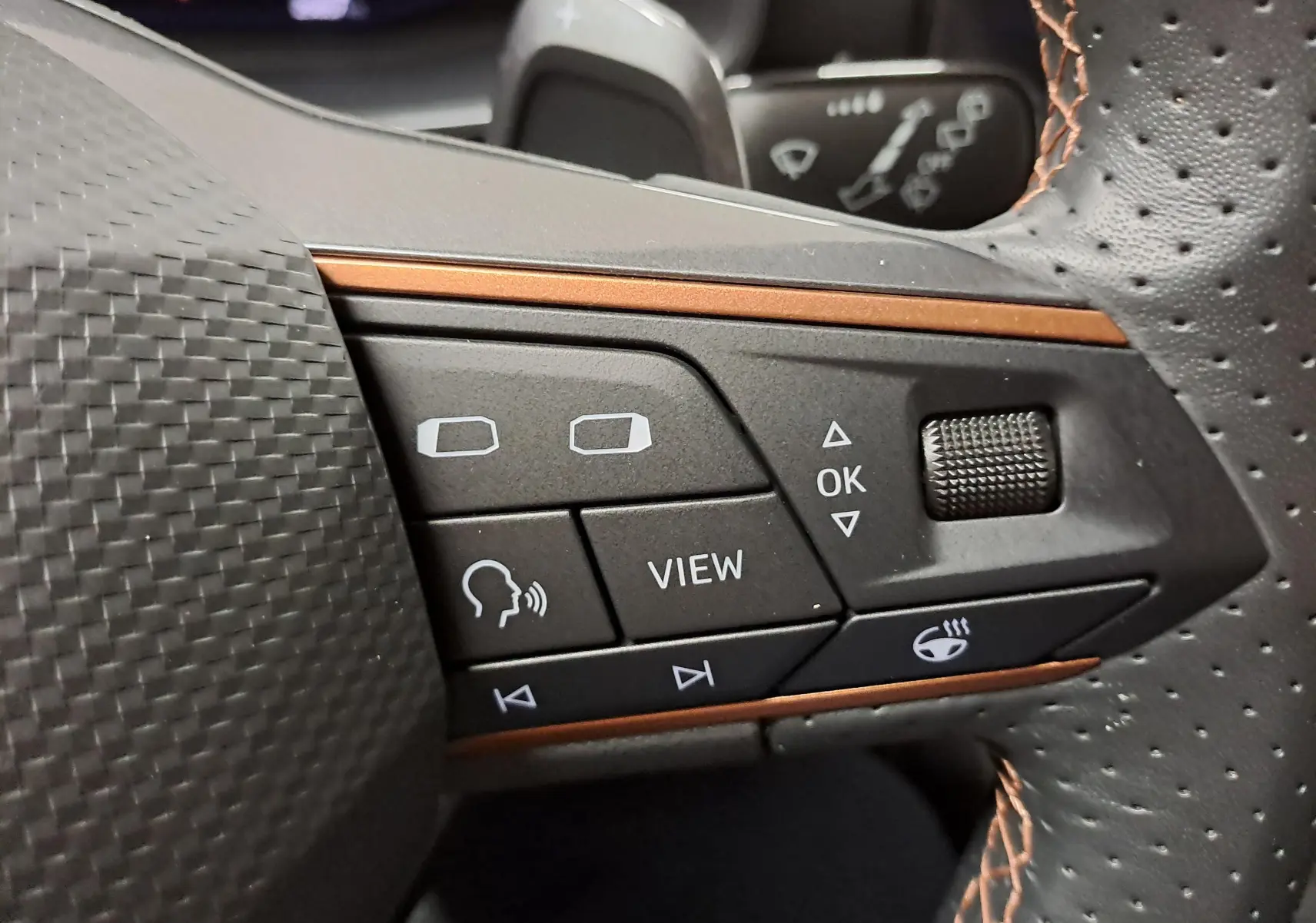 Gros plan sur les commandes du volant perforé avec surpiqûres cuivrées de la CUPRA Leon 2023 gris magnétique.