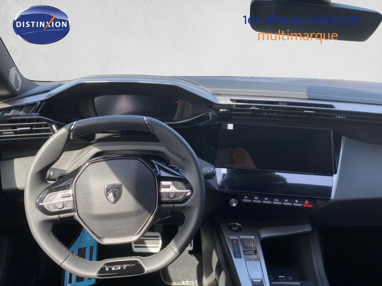 Vue intérieure centrée sur le volant GT et la console centrale noire d’une Peugeot 308 Hybrid blanche, modèle 2026.