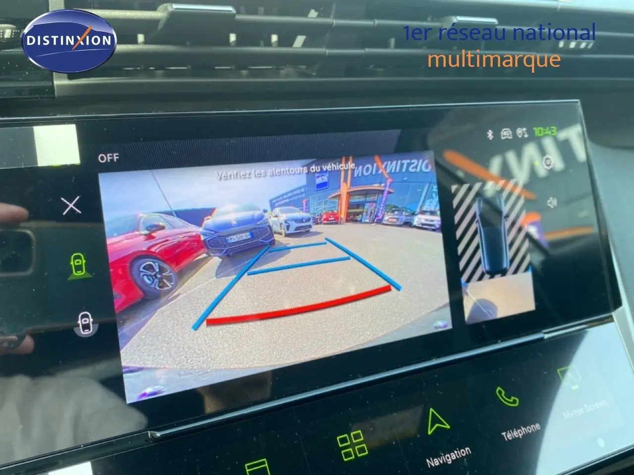Écran de caméra de recul montrant une Peugeot 308 blanche vue de l'arrière avec des voitures garées à côté.
