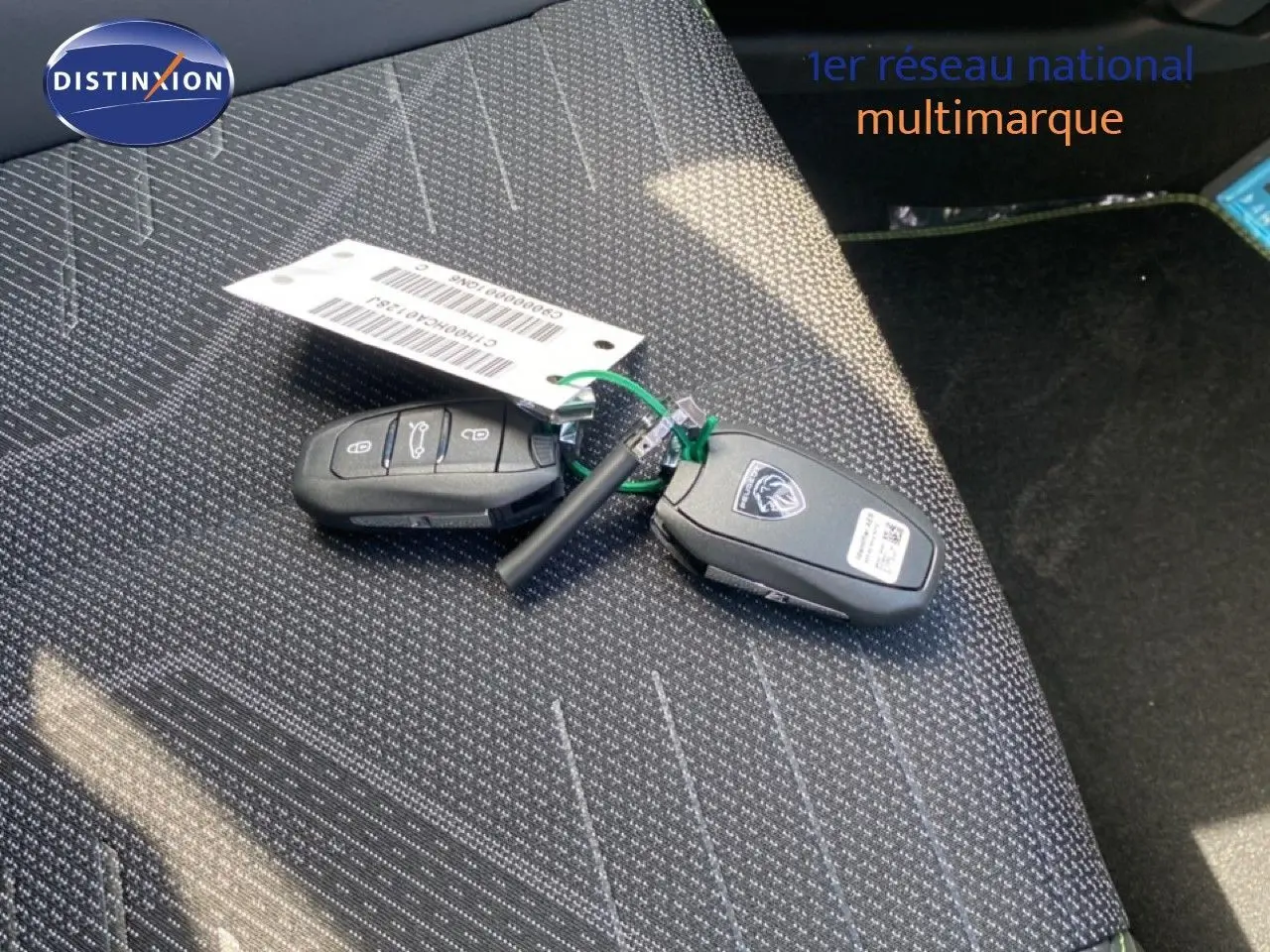 Clé de voiture Peugeot 308 Hybrid posée sur un siège tissu gris foncé à motifs, vue en plongée rapprochée.