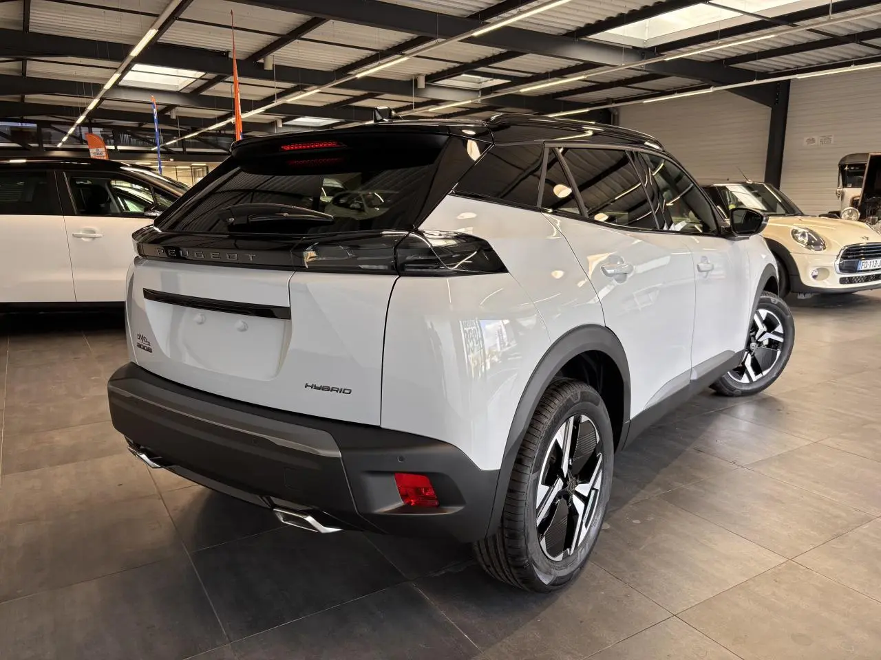 Vue 3/4 arrière droite du Peugeot 2008 blanc avec toit noir et double sortie d’échappement chromée en intérieur showroom.