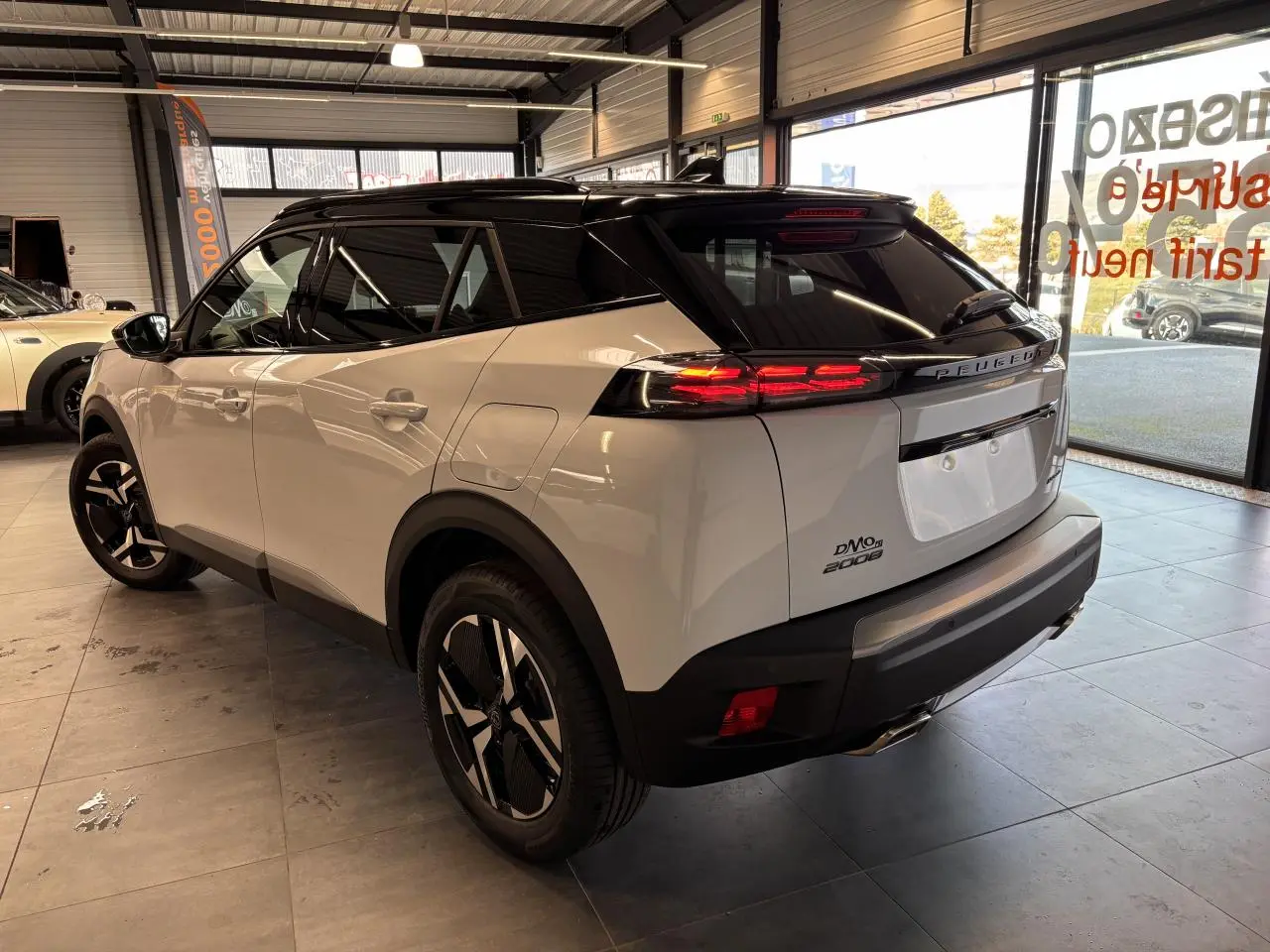 Vue 3/4 arrière droite du Peugeot 2008 blanc avec toit noir et feux arrière LED à 3 griffes dans un showroom.