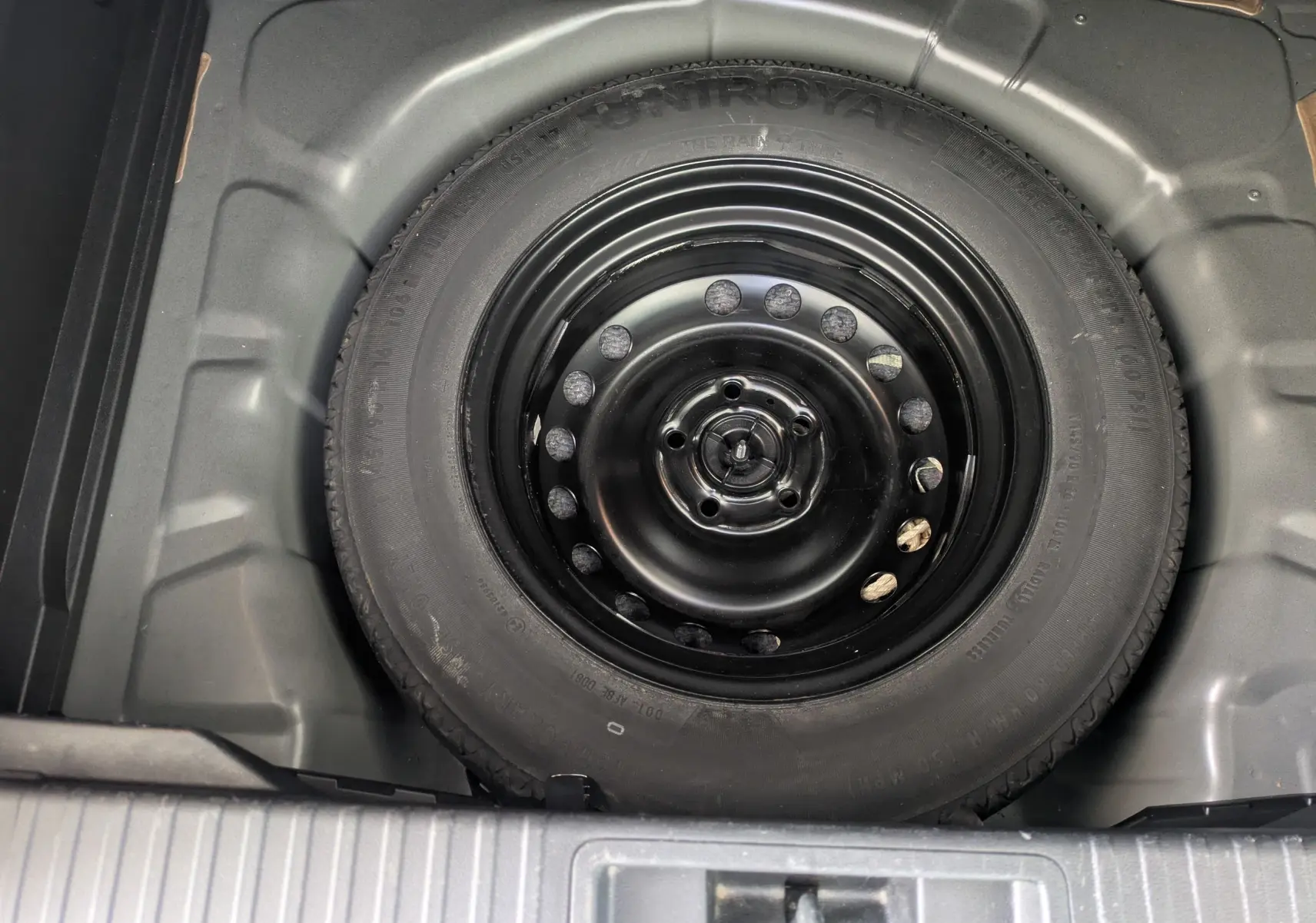 Vue plongeante sur la roue de secours noire logée dans le coffre du Renault Captur Business DCI 95 noir de 2020.