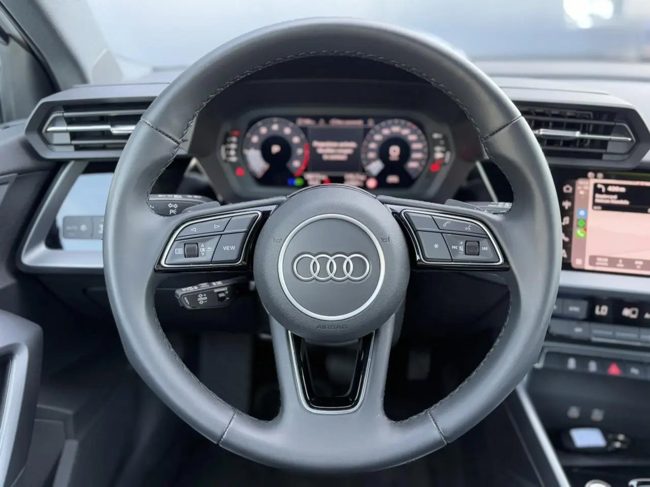 Volant cuir noir multifonctions Audi A3 Sportback 2024 vu de face avec tableau de bord numérique et écran tactile.