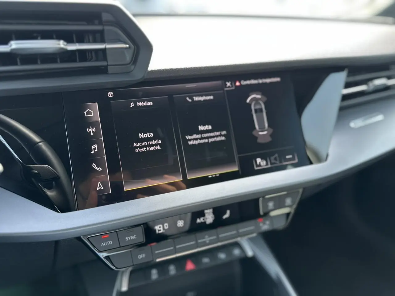 Vue rapprochée de la console centrale de l'Audi A3 Sportback 2024 blanche, avec écran tactile multimédia allumé.
