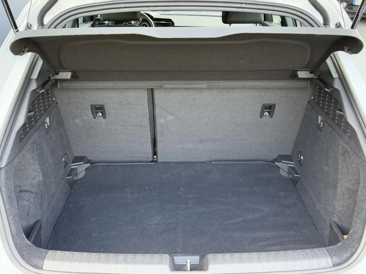 Coffre ouvert vu de l'arrière de l'Audi A3 Sportback blanc Arkona, espace de chargement vide et tapis gris.
