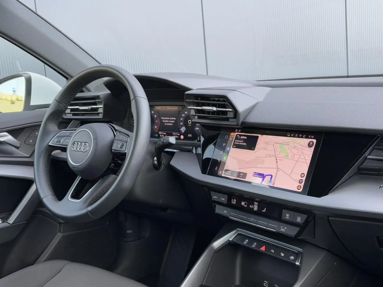 Vue intérieure côté conducteur de l'Audi A3 Sportback 2024, tableau de bord avec écran tactile de navigation allumé.