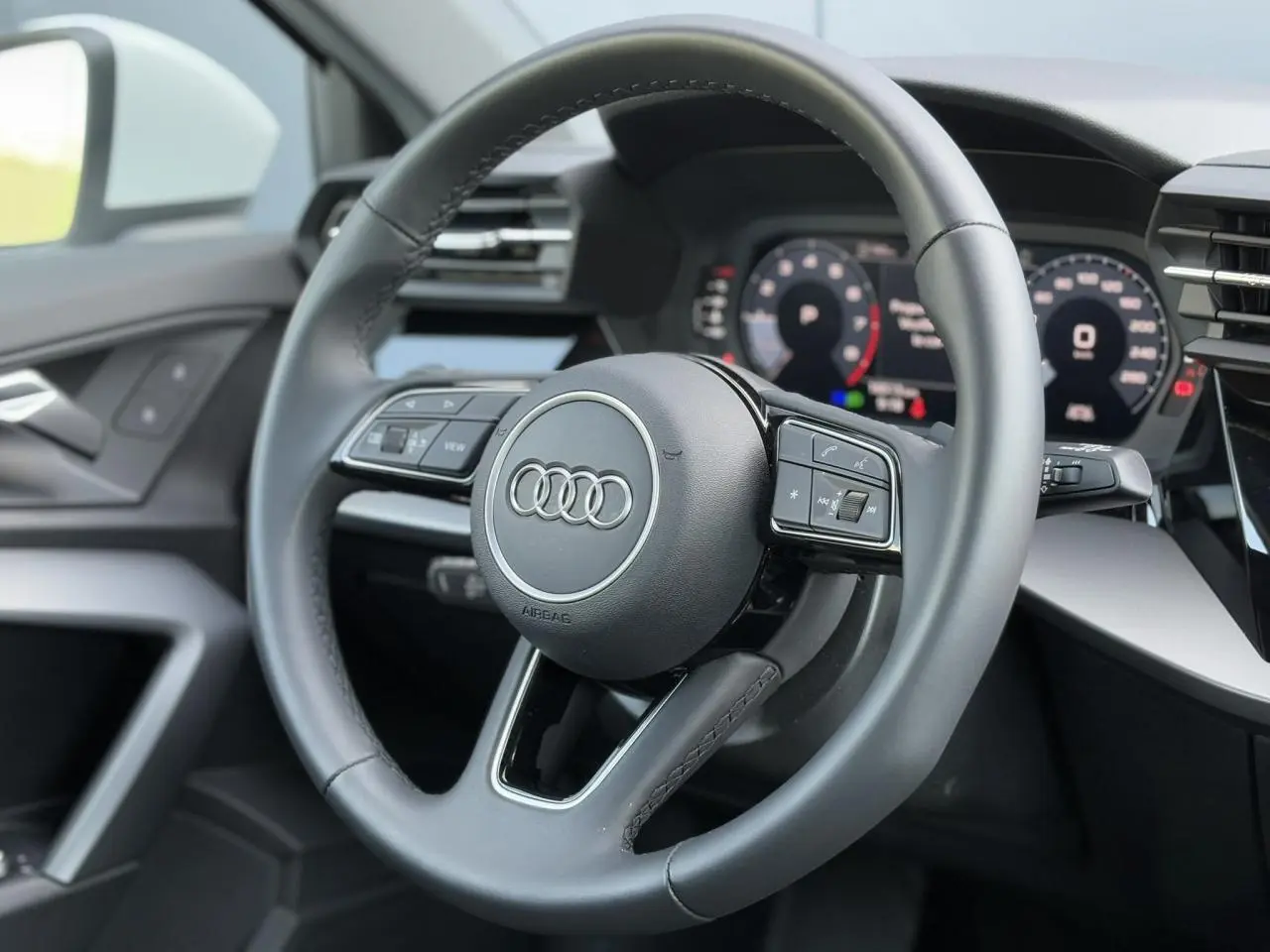 Vue rapprochée du volant cuir 3 branches multifonctions de l'Audi A3 Sportback 2024, intérieur noir moderne.