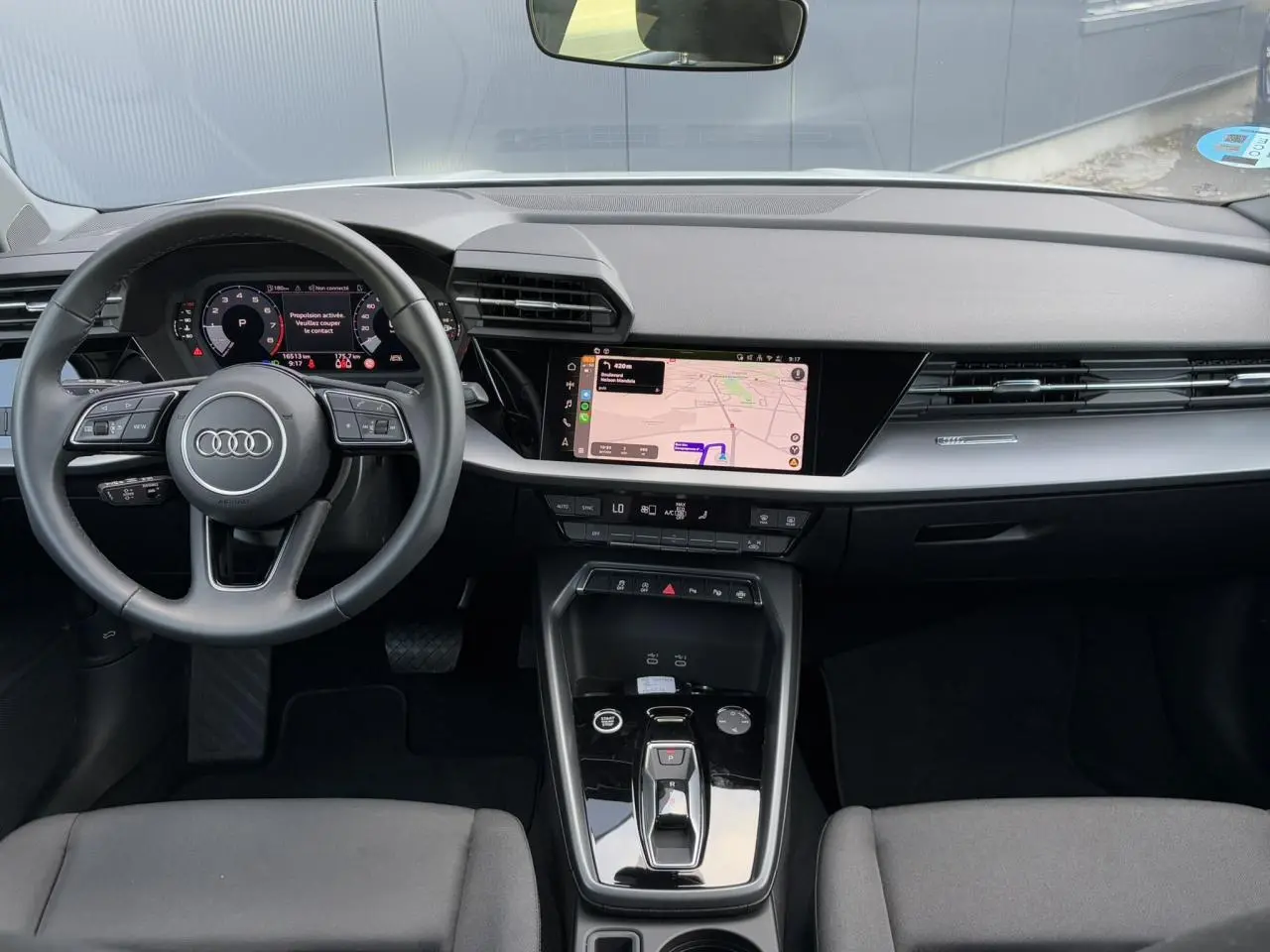 Vue intérieure avant de l'Audi A3 Sportback 2024, tableau de bord noir avec écran tactile et volant multifonctions cuir.