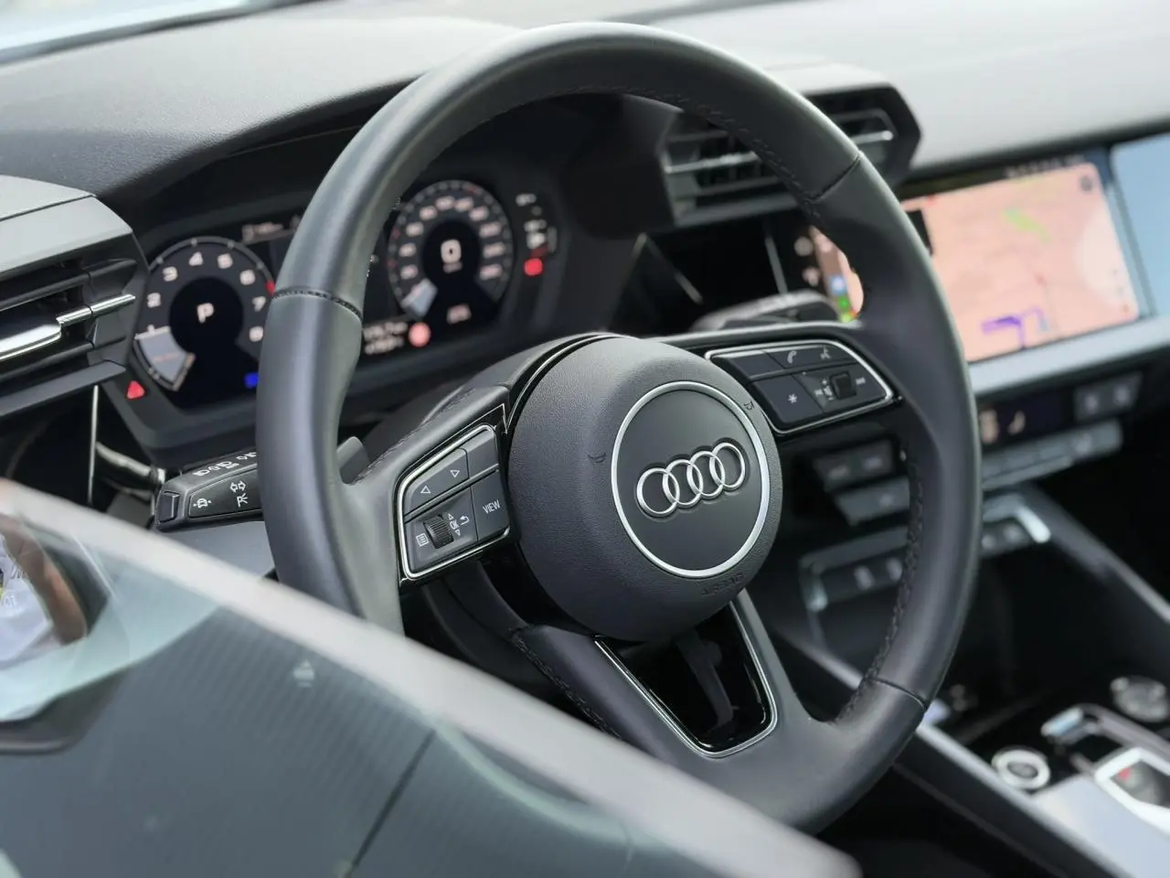 Vue rapprochée du volant cuir noir multifonctions d'une Audi A3 Sportback 2024 avec tableau de bord numérique et écran tactile.