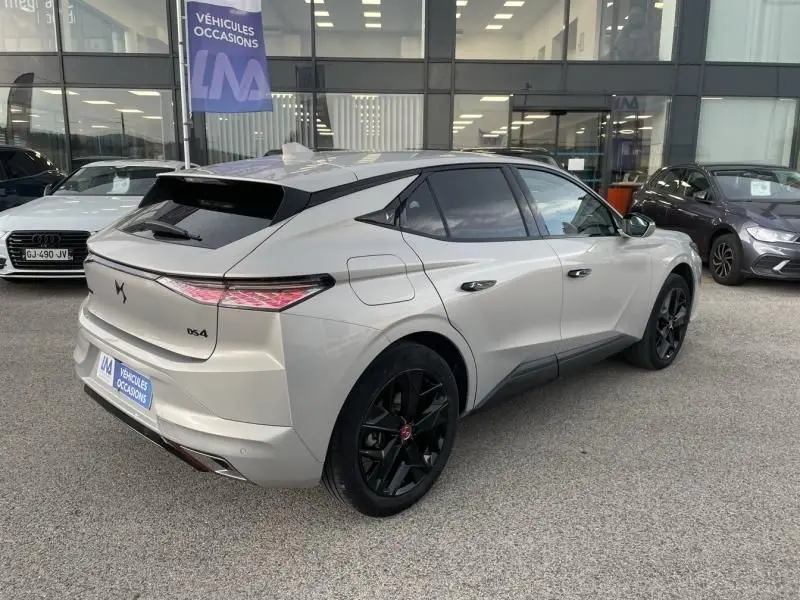 Vue 3/4 arrière droite d'une DS4 gris clair hybride rechargeable 2023 avec jantes noires et toit noir contrasté.