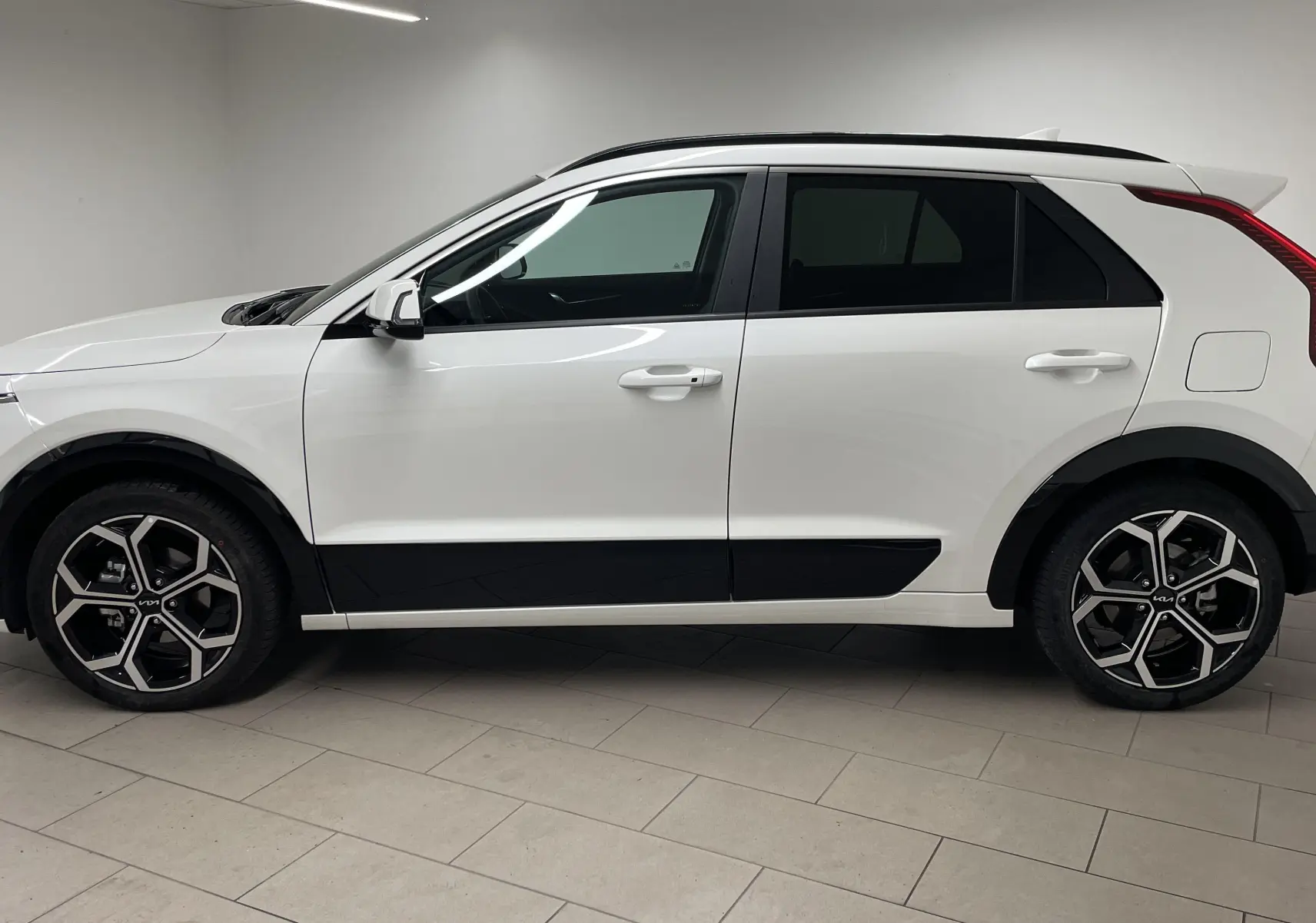 Vue de profil côté gauche du KIA NIRO 2025 blanc hybride avec jantes alliage noires et détails noirs contrastants.