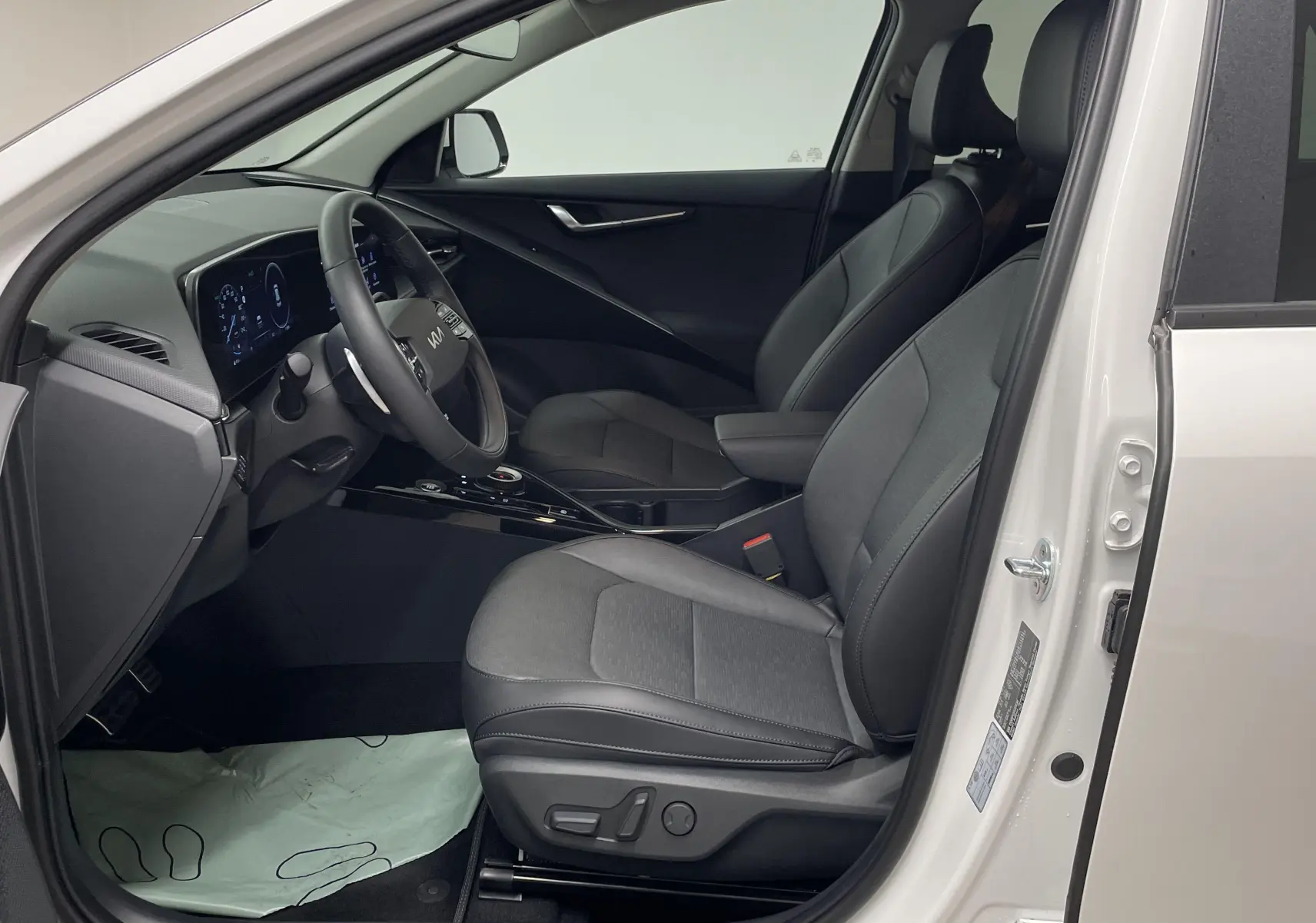 Intérieur côté conducteur du Kia Niro blanc 2025, sièges noirs et tableau de bord digital moderne visible.