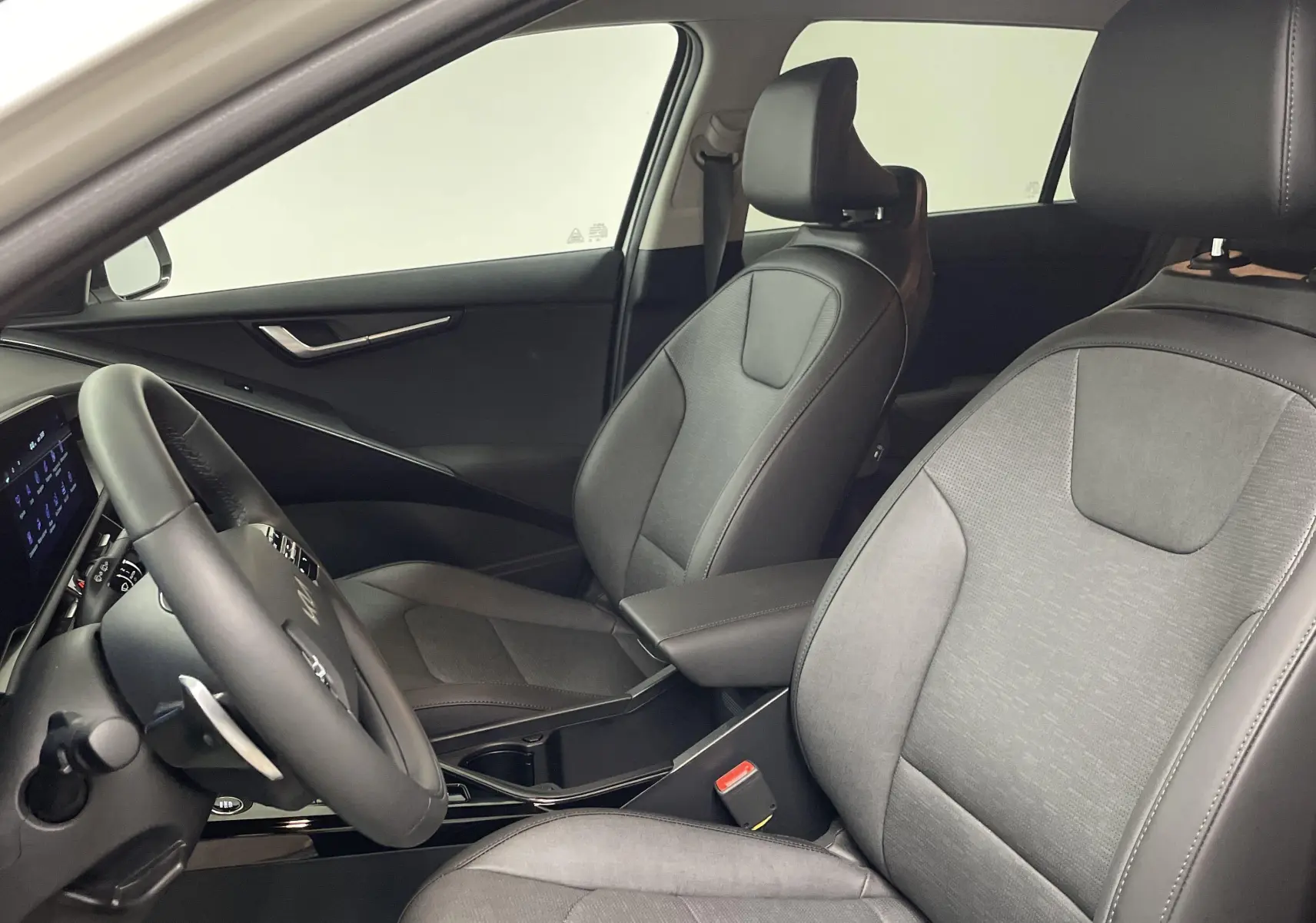 Intérieur du Kia Niro 2025 blanc, vue côté gauche sur les sièges avant en tissu gris et le volant multifonction.