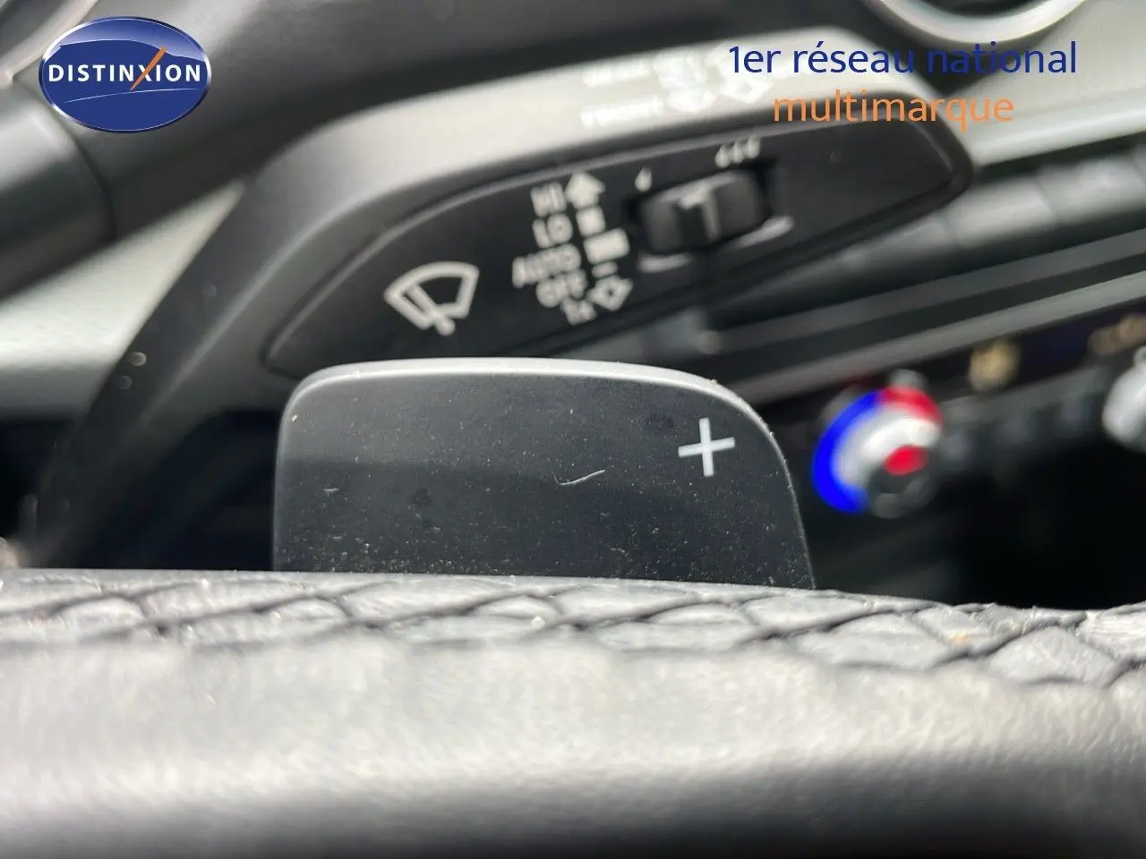 Gros plan sur la palette de changement de vitesse droite du volant d'un Audi Q2 noir Mito Metal, avec commandes de climatisation en arrière-plan.