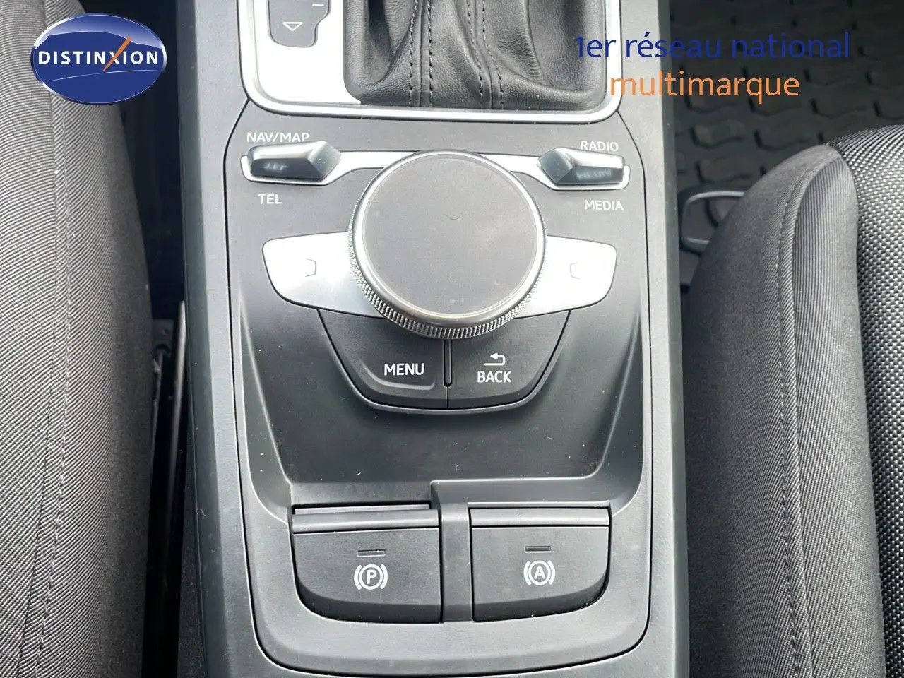 Vue rapprochée de la console centrale noire de l'Audi Q2 2023, mettant en valeur les commandes multimédia et le frein à main électrique.