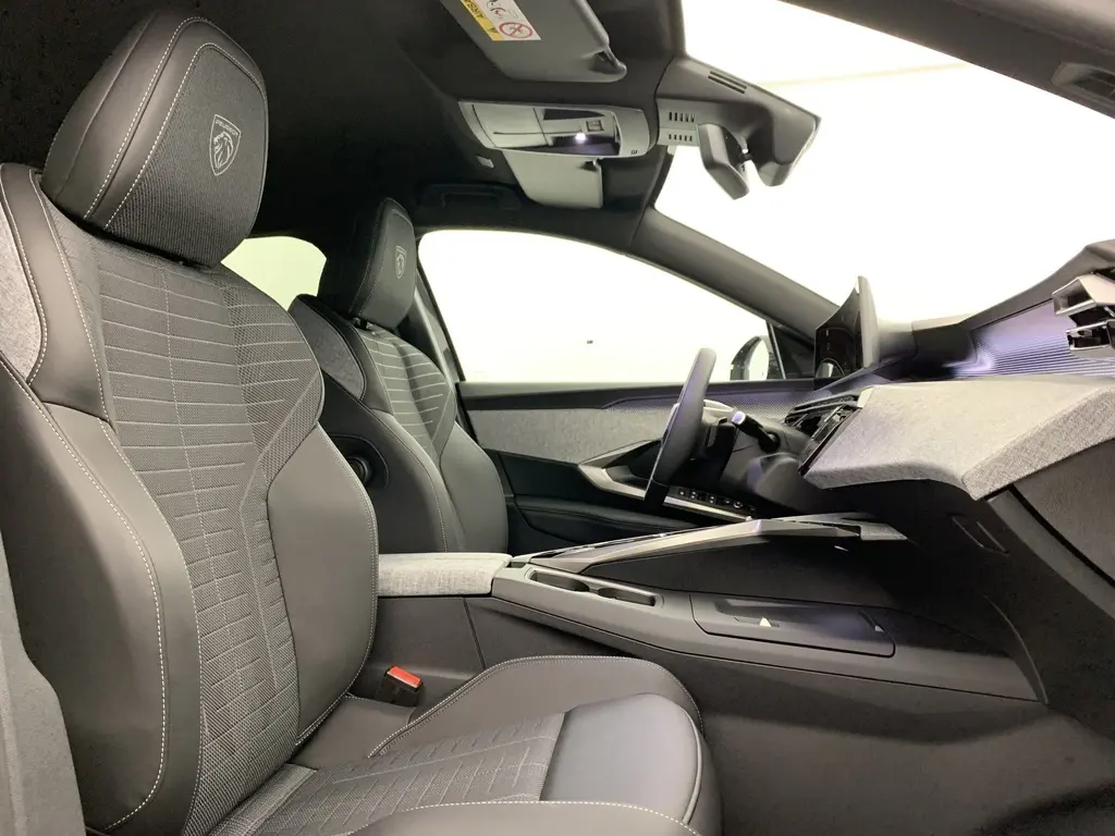 Vue intérieure côté conducteur du Peugeot 3008 Hybrid 145 GT avec sièges tissu et cuir noir, planche de bord moderne et écran panoramique.
