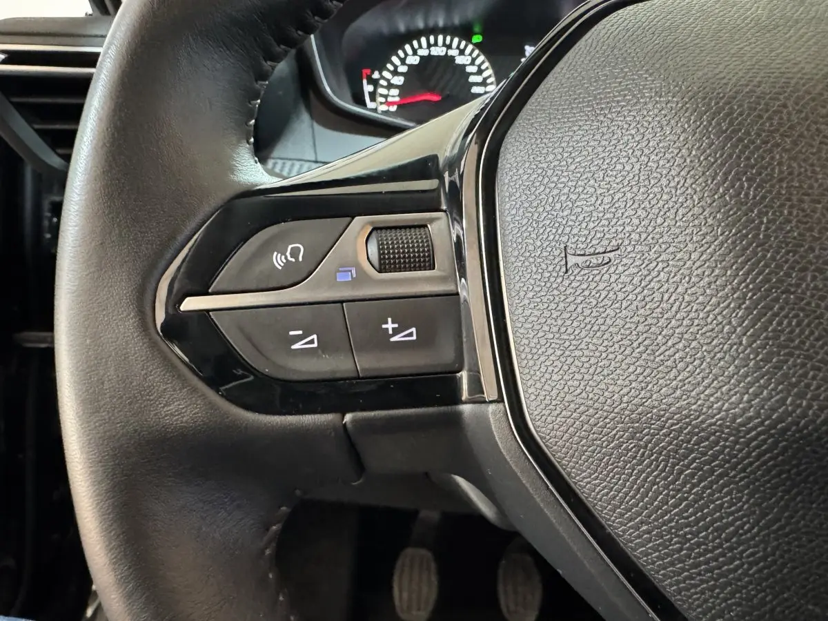 Gros plan sur le volant cuir noir du Peugeot 2008 2022, côté gauche avec commandes audio et tableau de bord partiel.
