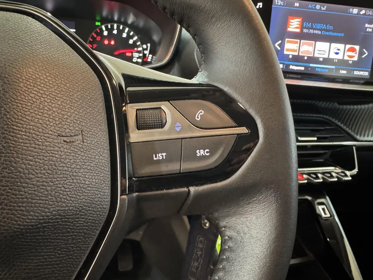 Gros plan sur le volant cuir noir de la Peugeot 2008 2022, avec commandes audio et écran tactile du tableau de bord visible.