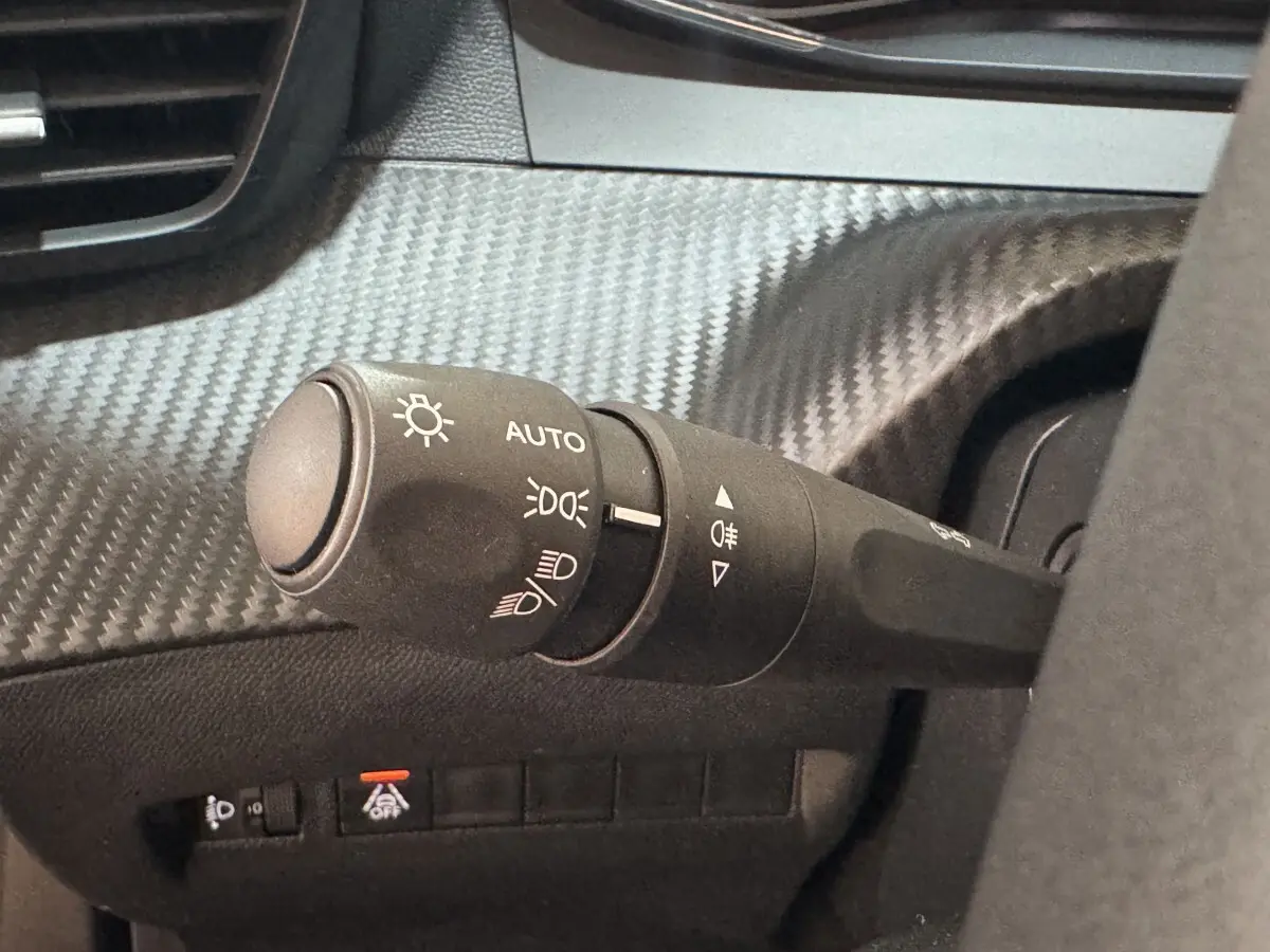Gros plan sur la commande des phares à gauche du volant dans l’habitacle noir du Peugeot 2008 PureTech 130 S&S ACTIVE PACK.