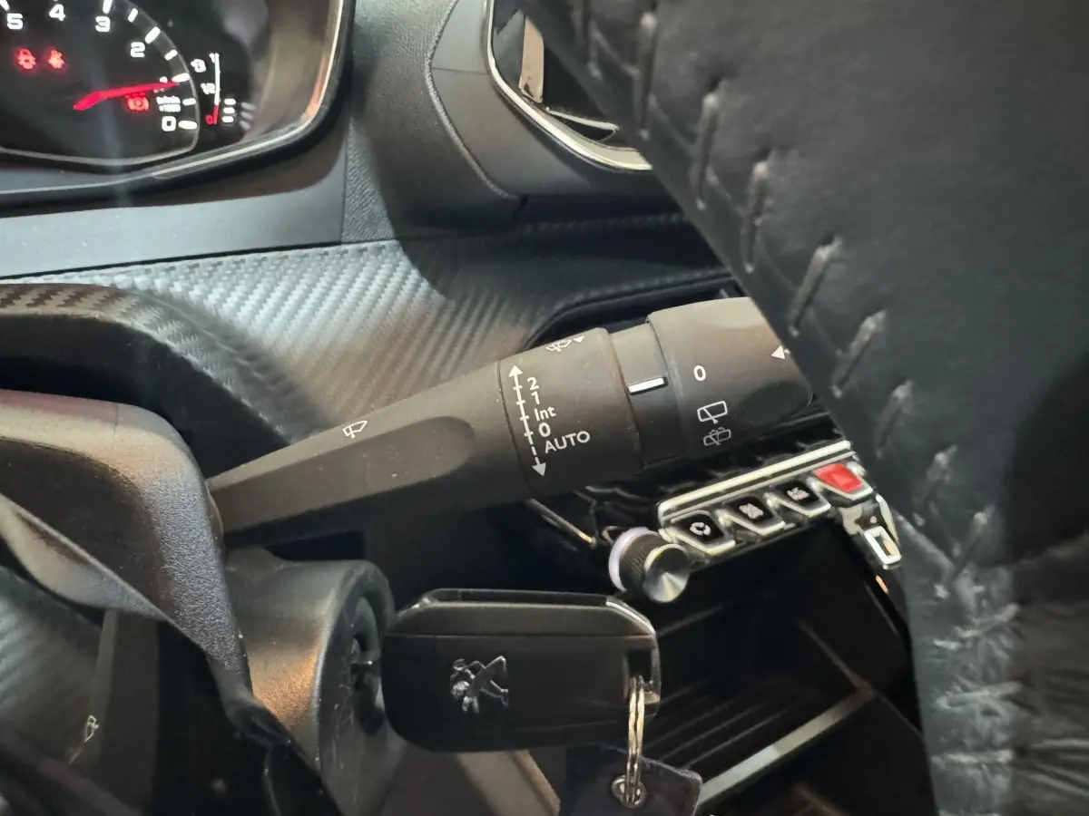 Gros plan sur le volant cuir noir et la commande d’essuie-glace du tableau de bord du Peugeot 2008 noir 2022.